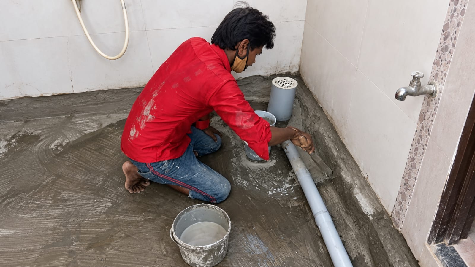Worker sealing the floor drain and pipe penetration in a sunken bathroom floor