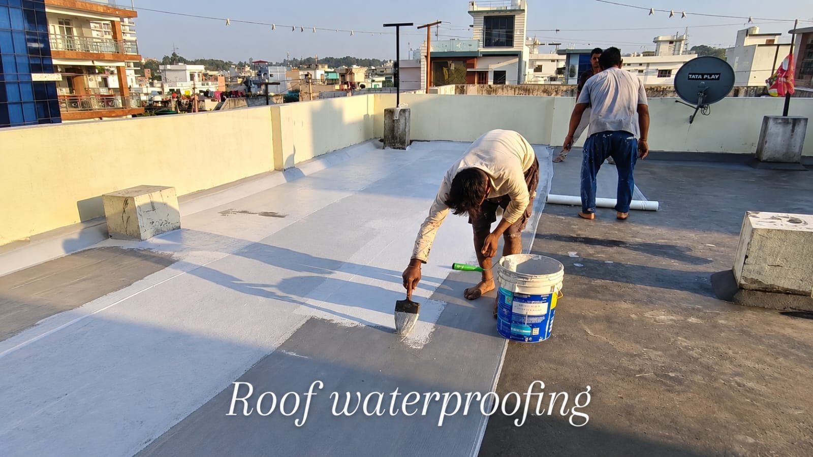 Applicator brush-coating a terrace slab with waterproofing membrane at dusk