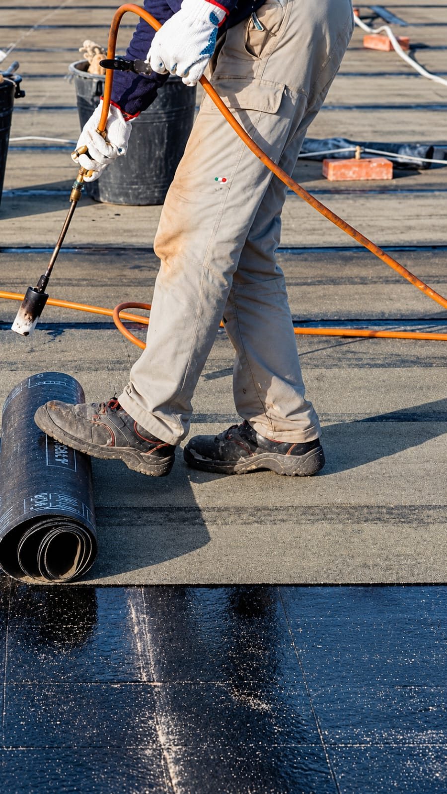 Applicator torch-fusing a bitumen waterproofing membrane roll onto a rooftop slab